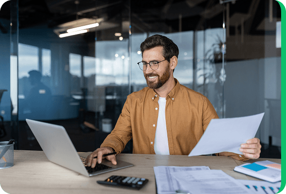 Smiling man working on a laptop in a modern office, comparing energy contracts online.